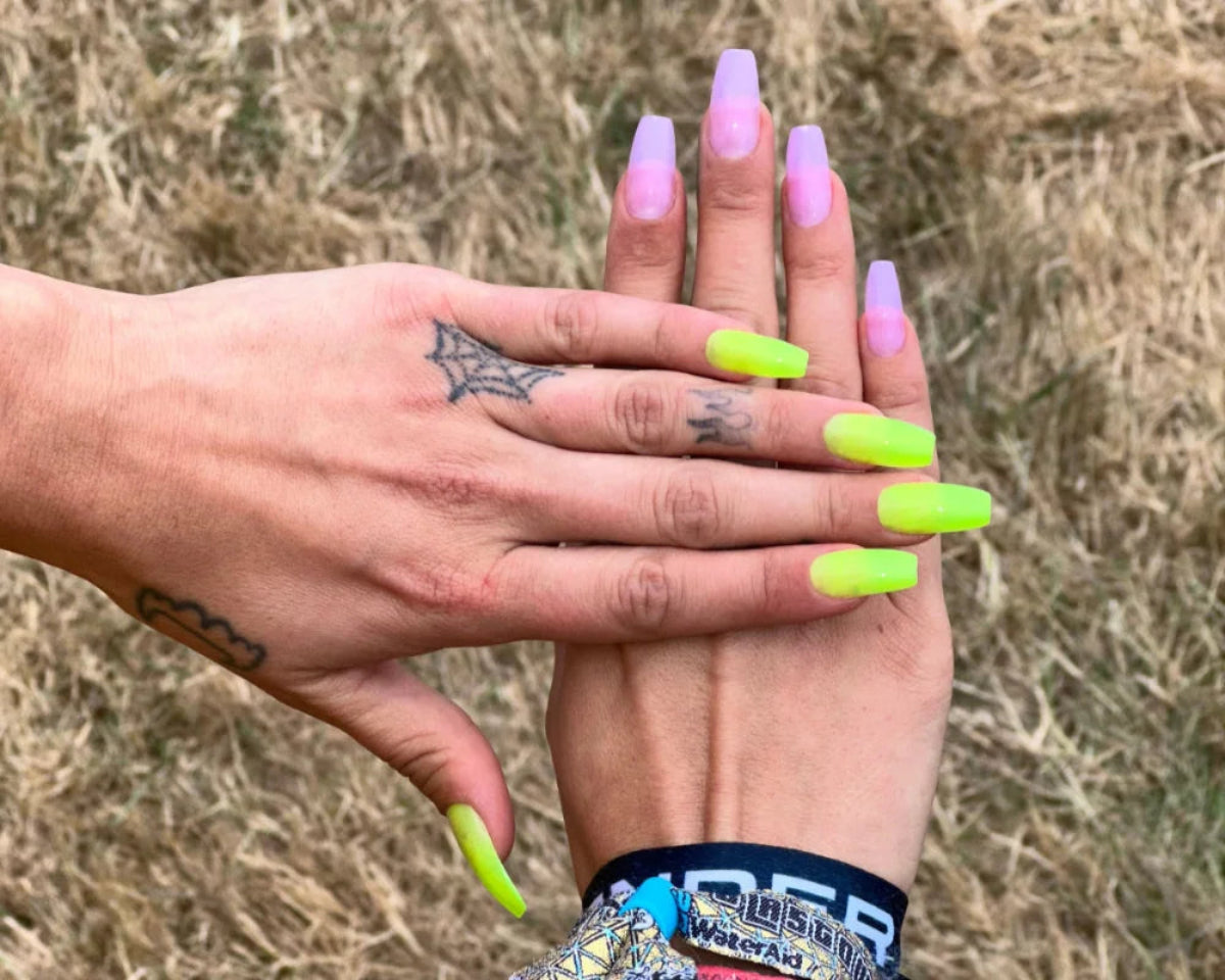 Two hands with neon green and pink nail polish against a blurred natural background