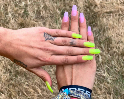 Two hands with neon green and pink nail polish against a blurred natural background
